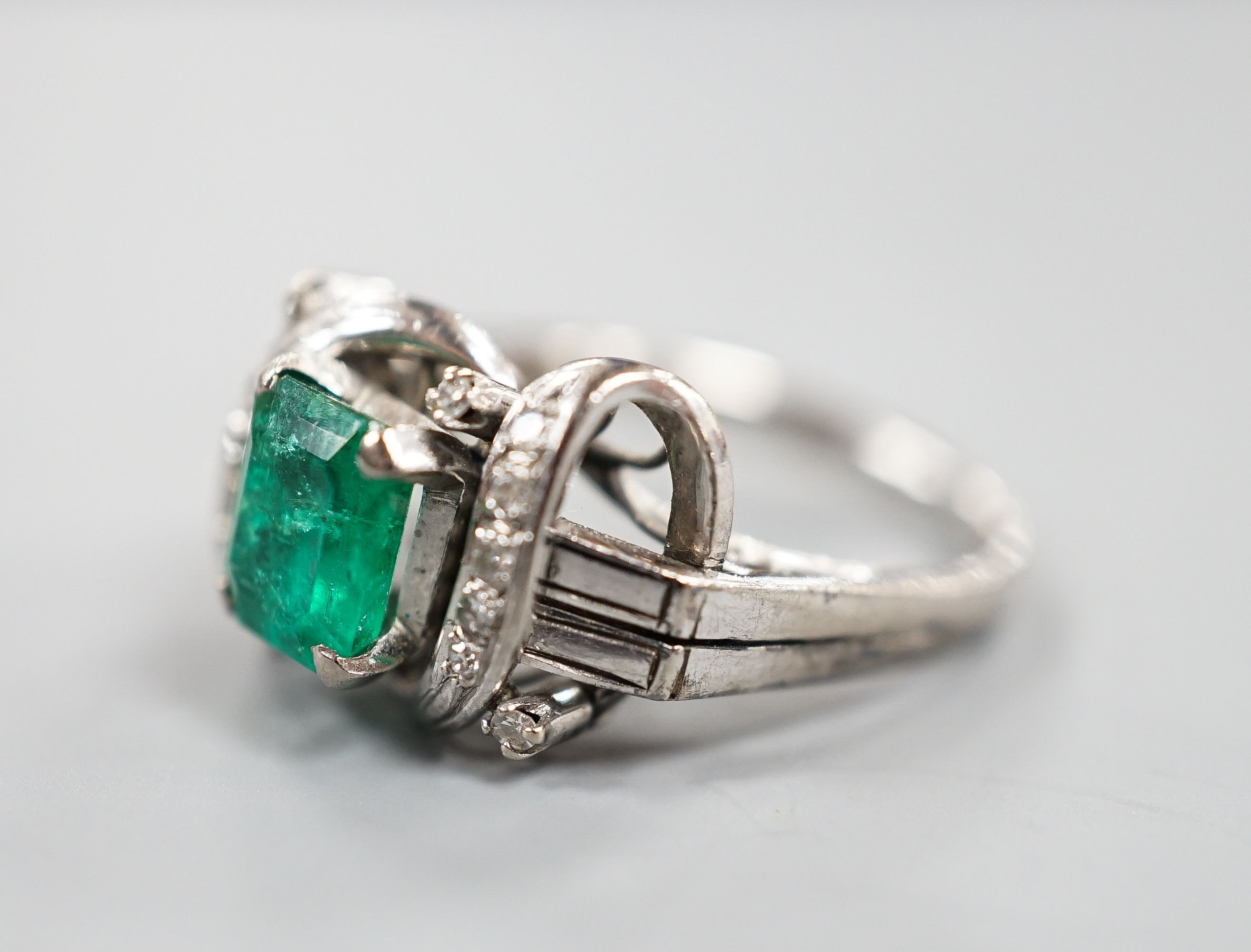 A modern 14k white metal and single stone emerald ring, with diamond chip set scroll setting, size K/L, gross weight 4.5 grams.